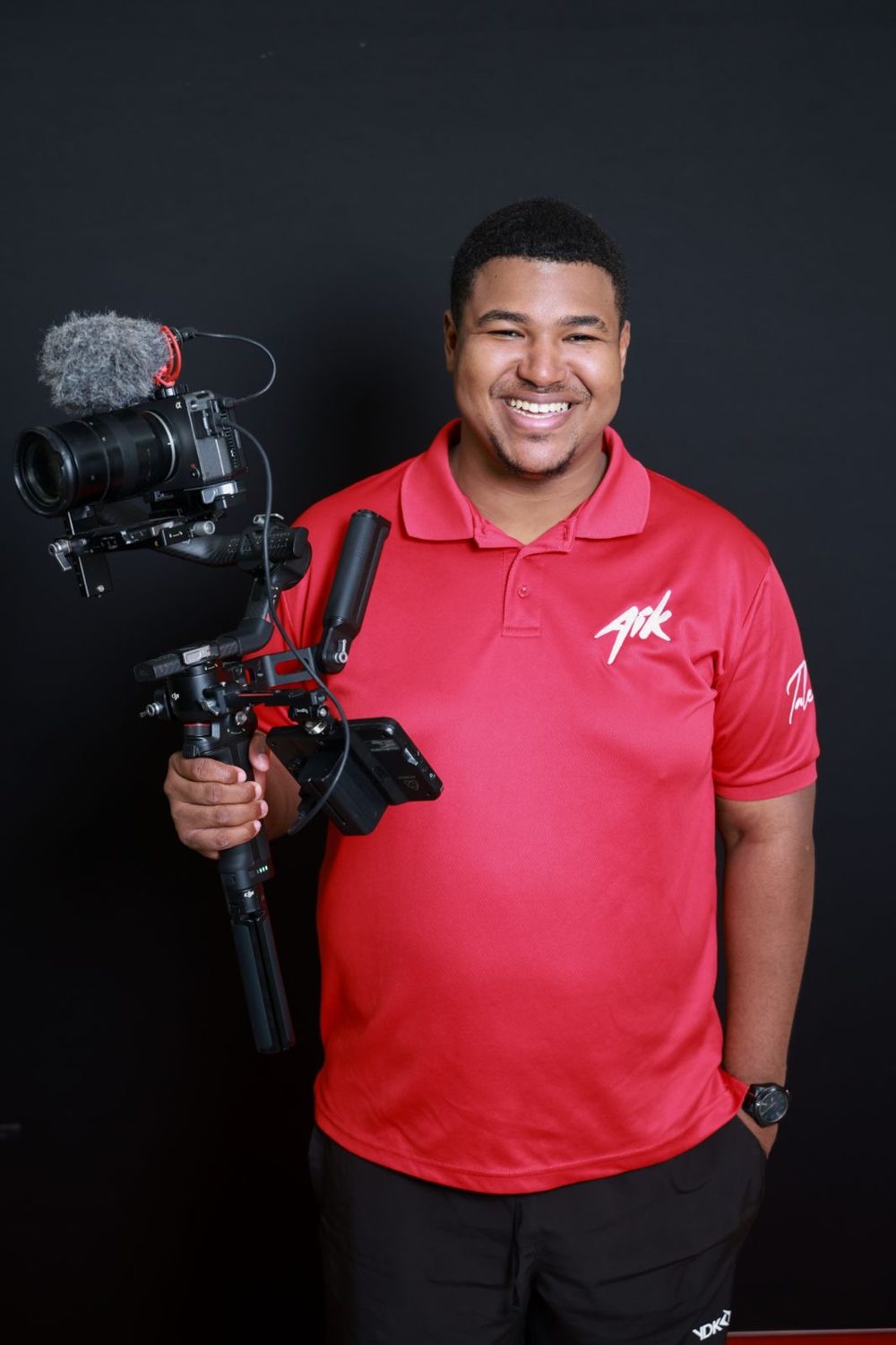 Joshua Ortega holding a camera rig on a gimbal, wearing a red Arte i Kultura polo