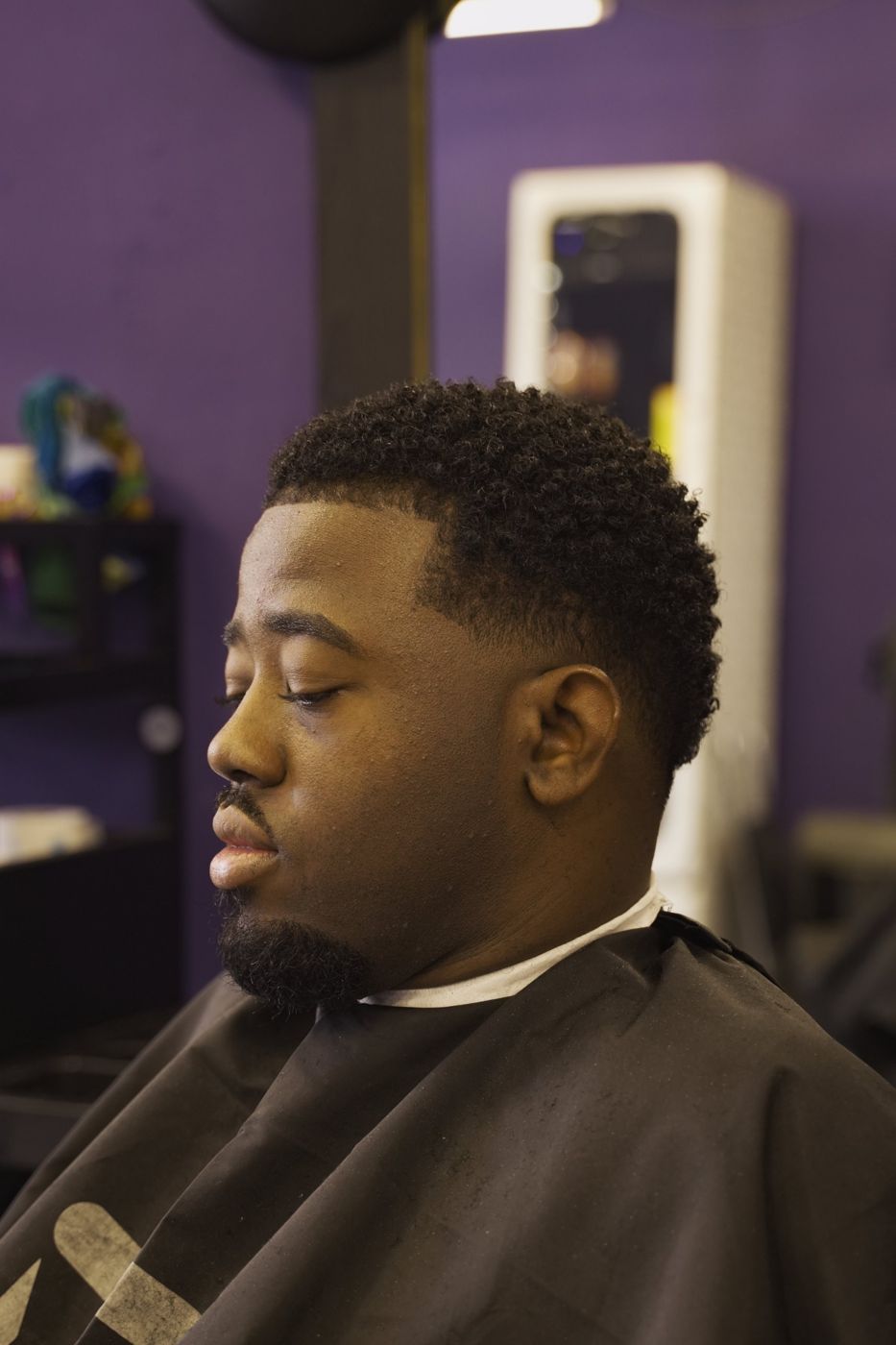 Client in profile after a fresh fade, purple barbershop wall behind